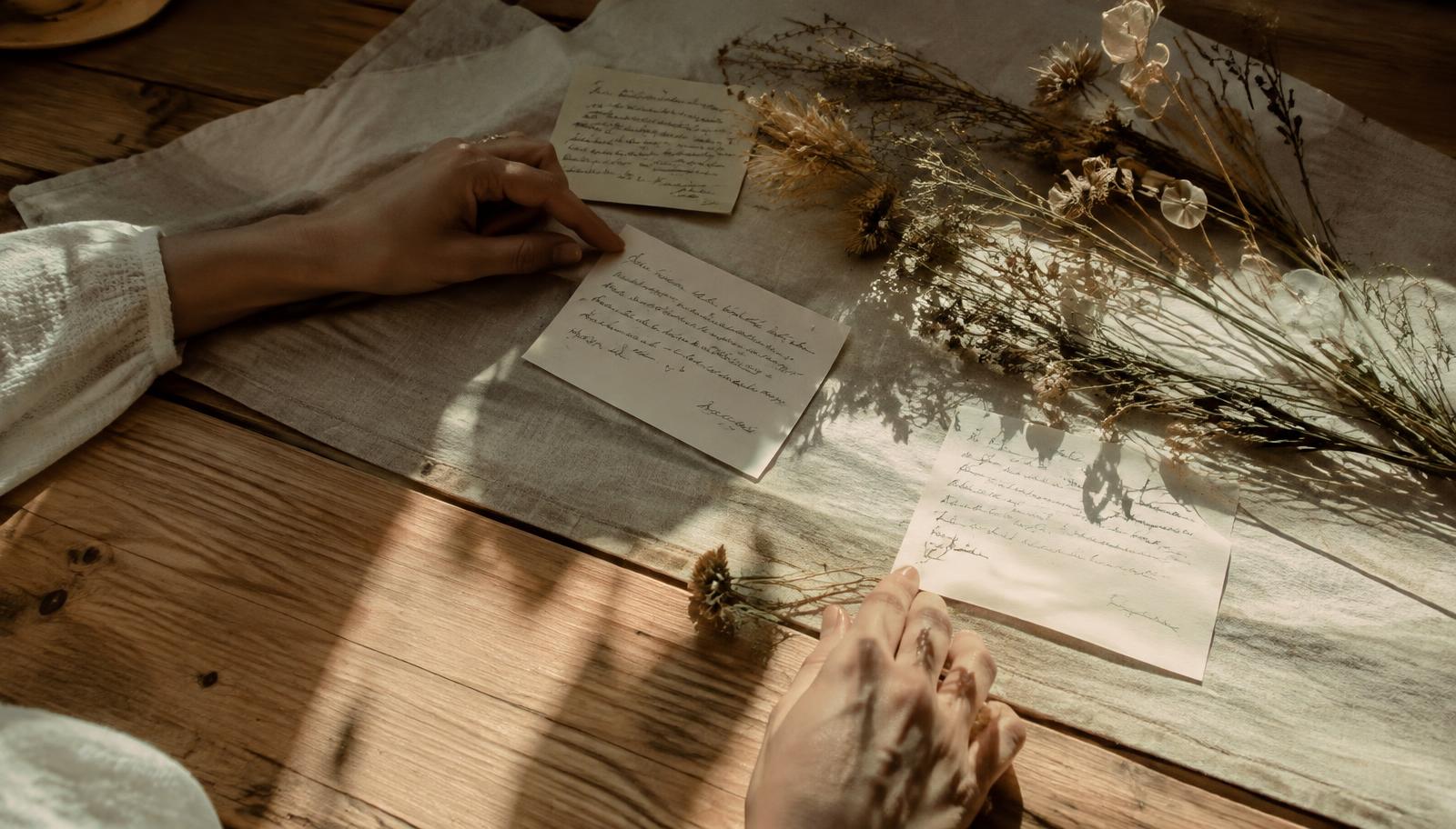 Hands arranging handwritten notes and dried grasses in afternoon light